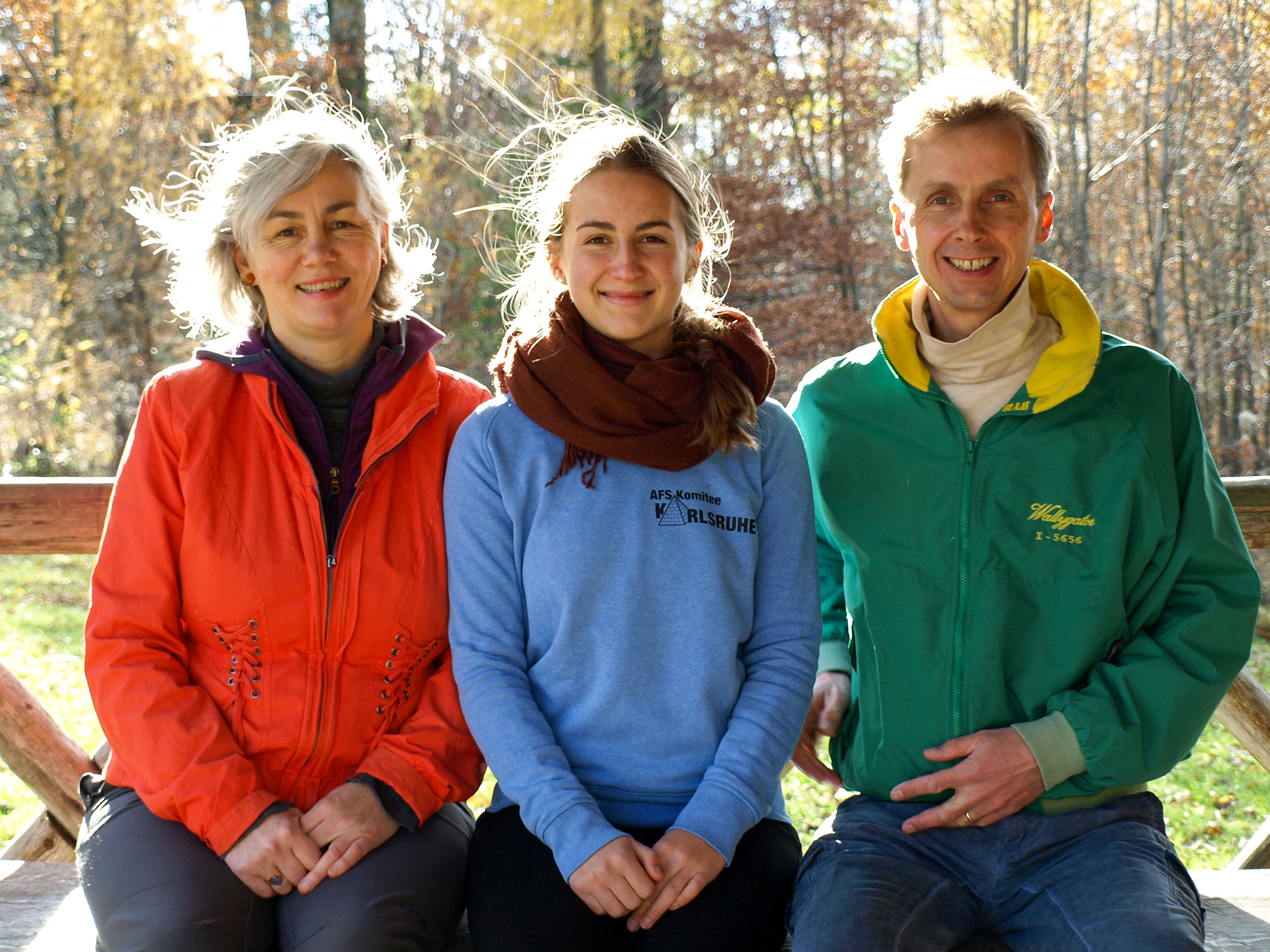 Die Gastgeber des Bahnwärterhauses im Vogtland sitzen gemeinsam vor herbstlicher Waldkulisse