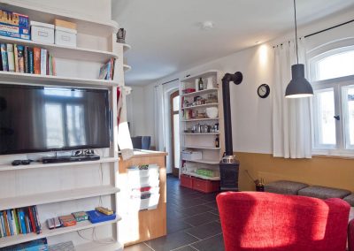 Gemütlicher Wohnbereich mit Ofen, Fernseher und Bücherregal im Bahnwärterhaus