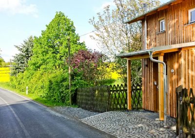 Eingang des Bahnwärterhauses mit Holzfassade und Pflasterweg im Grünen